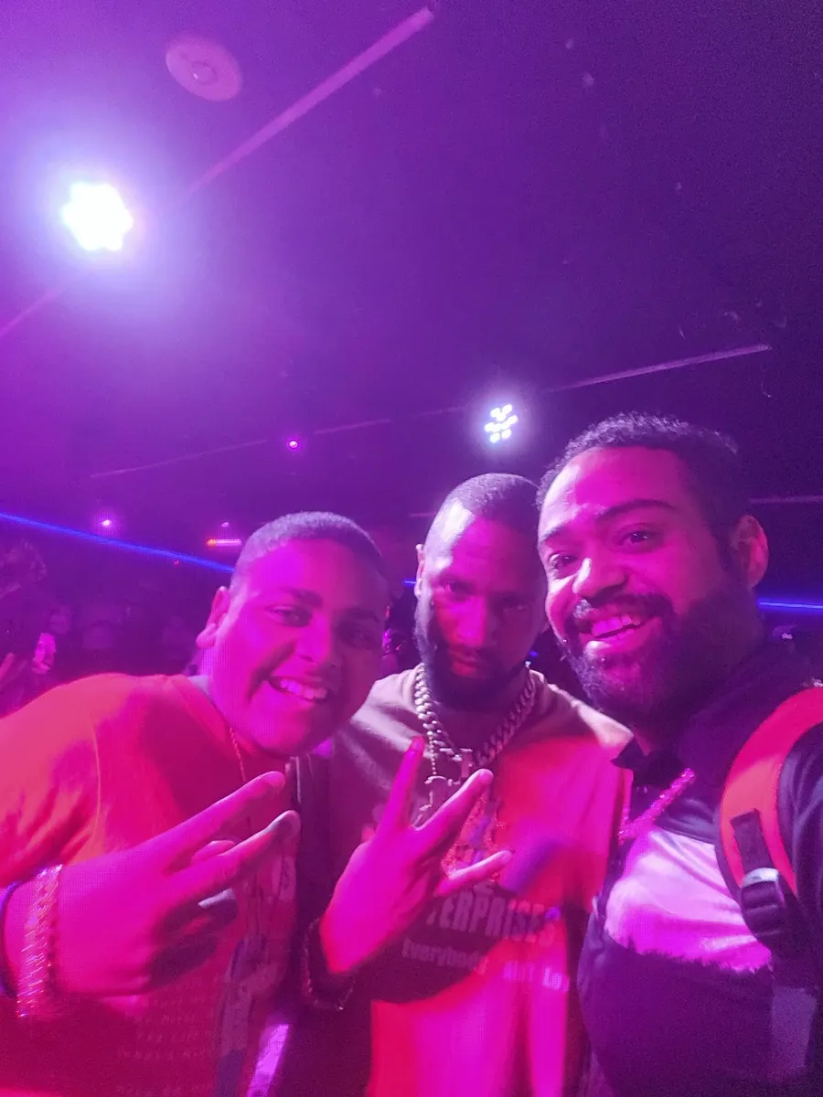 JC with two other guests, all throwing peace signs under pink lights at a BET weekend event